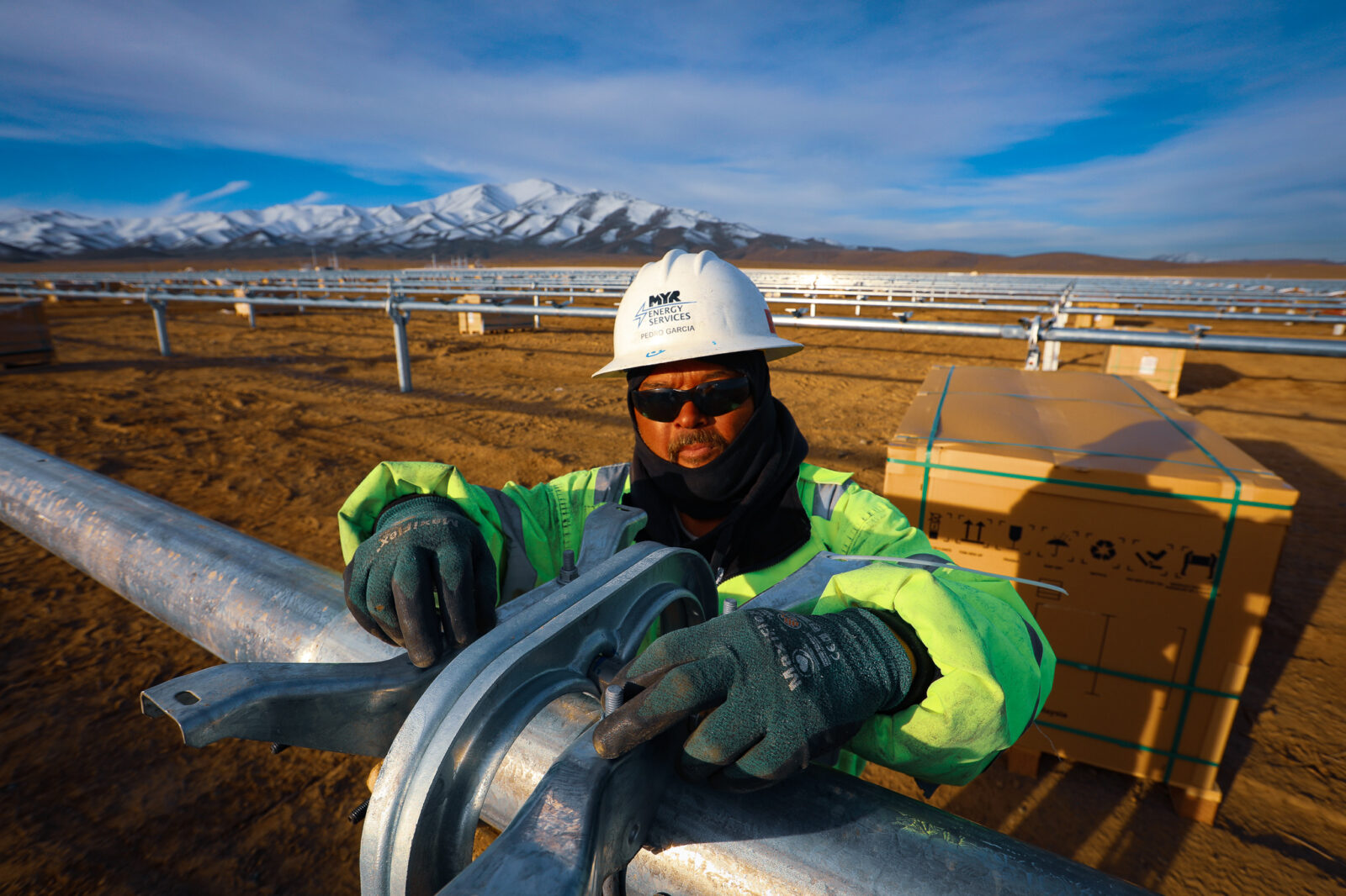 ͵E Energy employee prepares for solar panel installation with snowcapped mountains in the distance
